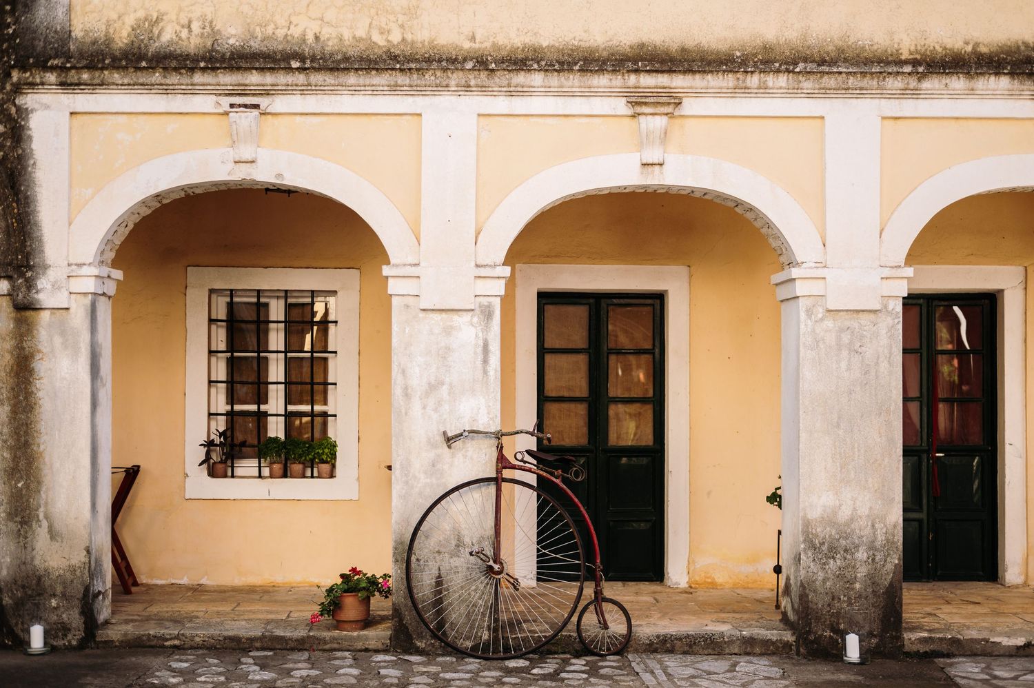 Historic yellow colonial building facade with arched walkways and vintage penny-farthing bicycle on display.
