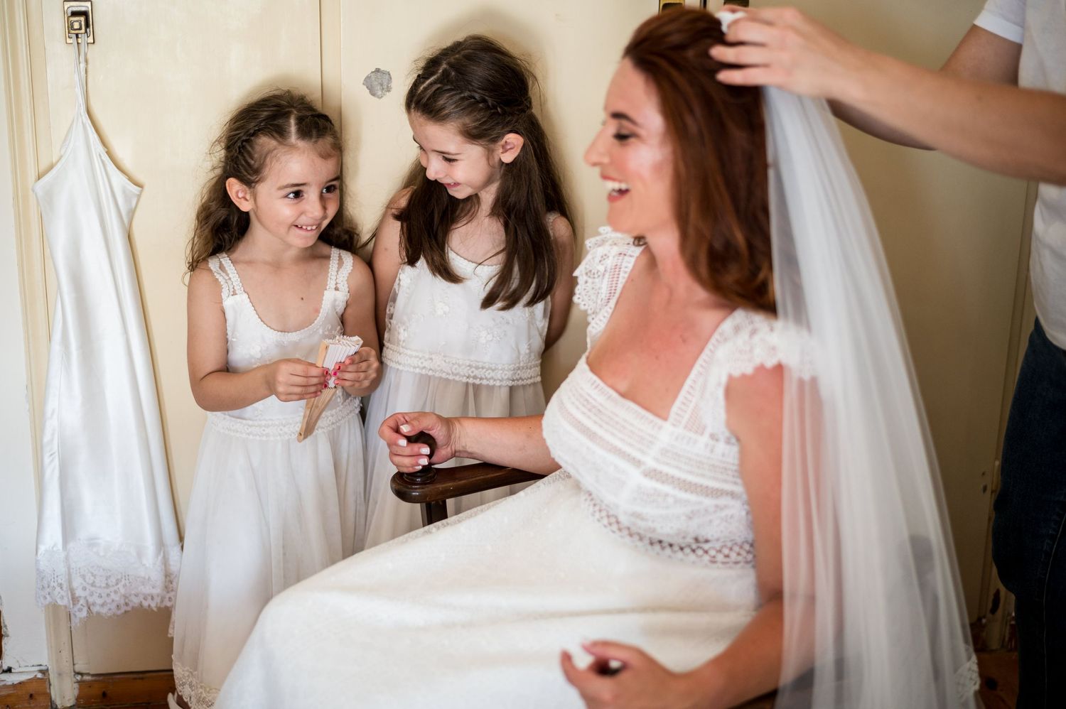 Wedding party members help with final preparations in a sunlit room.