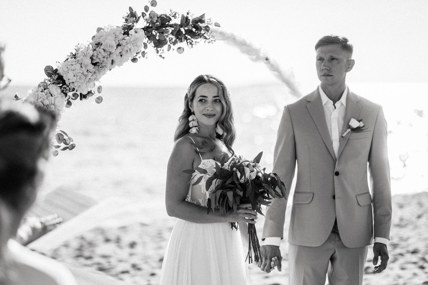 A romantic beach wedding ceremony with a floral arch and ocean backdrop.