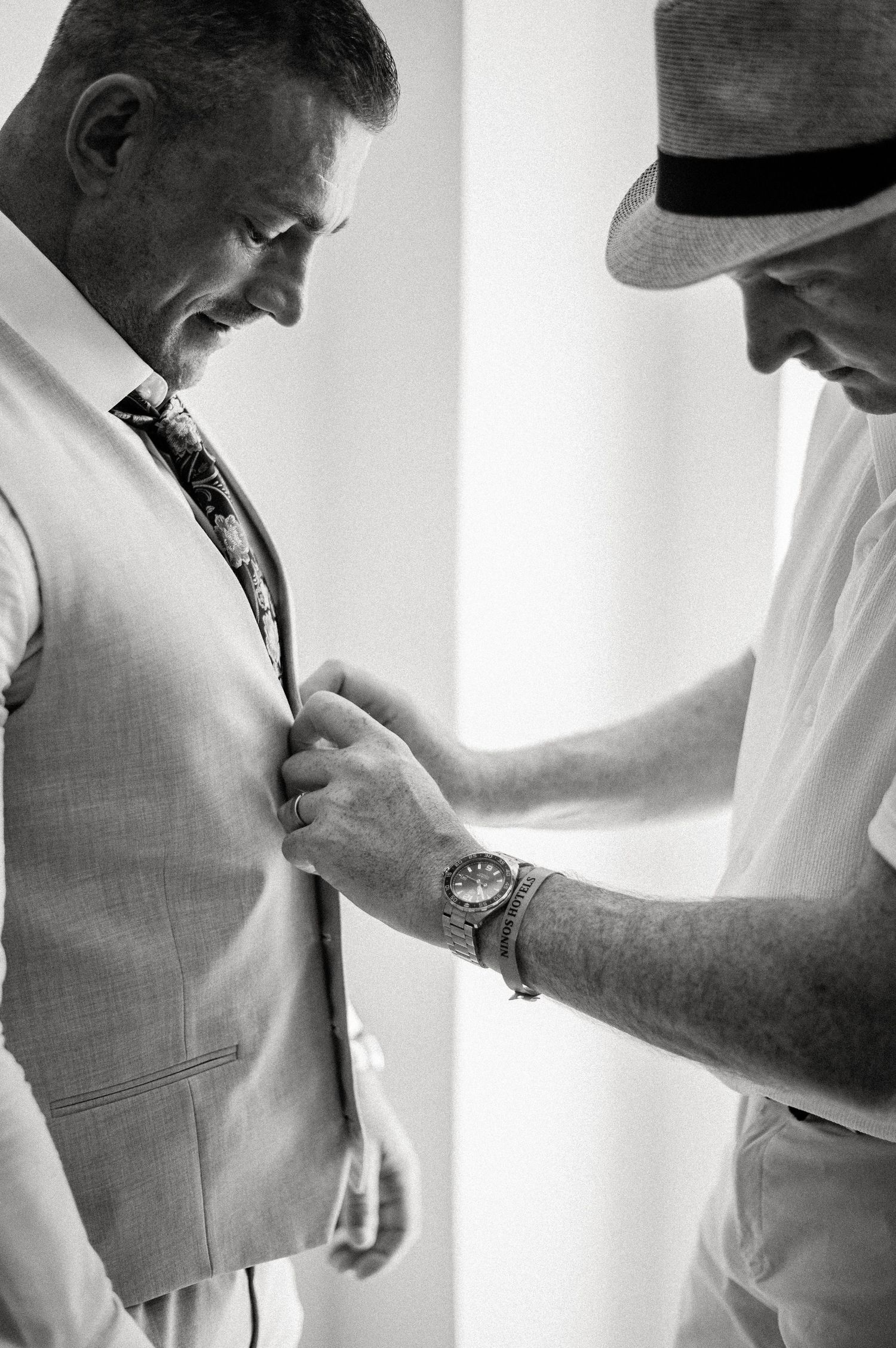 Black and white photo capturing final adjustments of formal wedding attire and accessories.