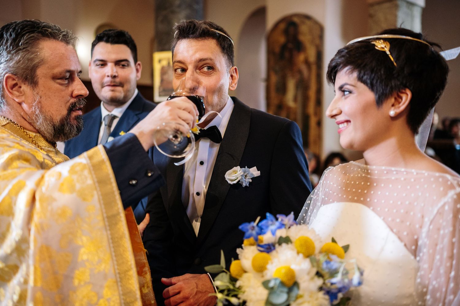 Wedding ceremony in progress with golden religious vestments and decorative floral arrangements.