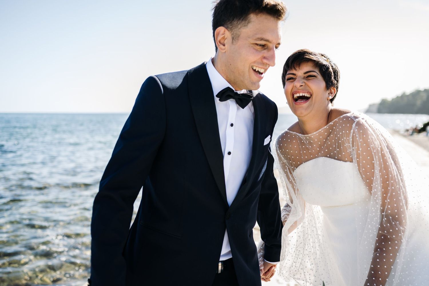 A joyful wedding couple shares candid moments by the seaside.