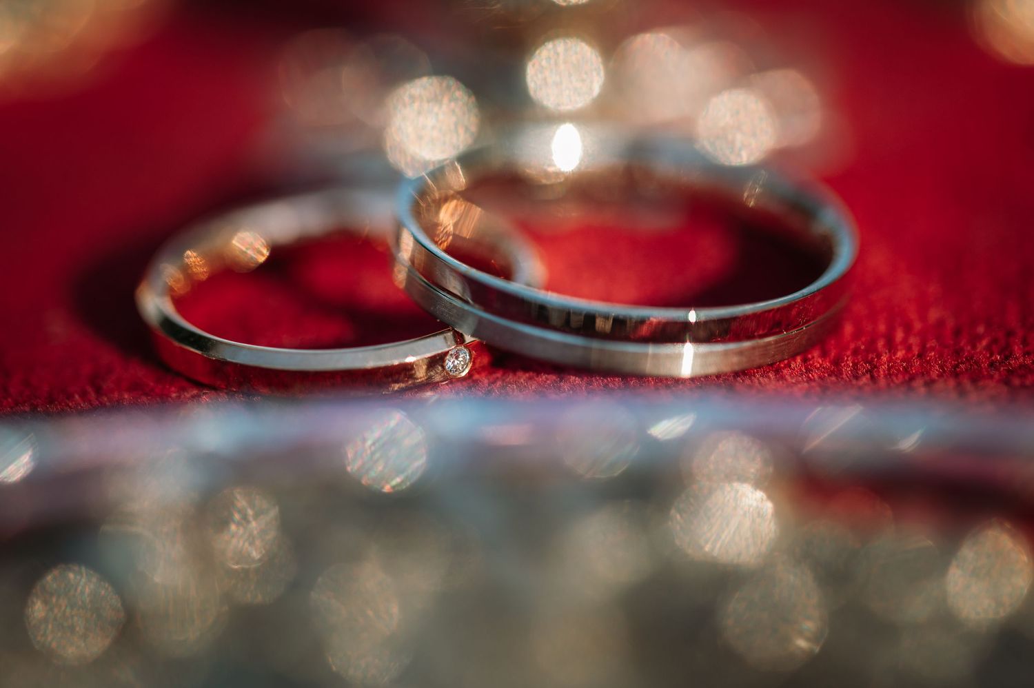 Wedding rings sparkle against a red background with beautiful bokeh lighting effects.