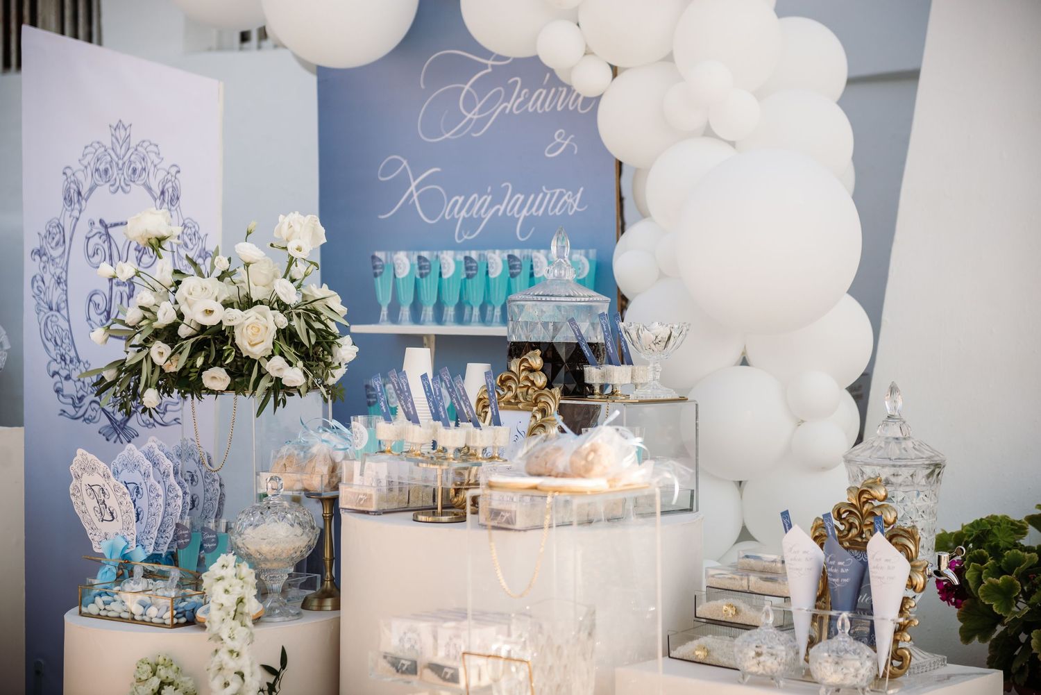 White balloon arch and elegant dessert table setup with blue and white wedding decor.