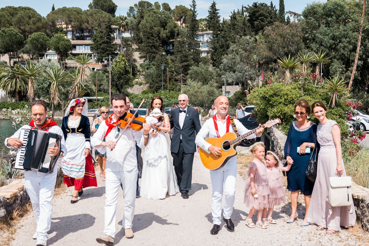 Wedding guests in formal attire gather for outdoor celebration by the water.