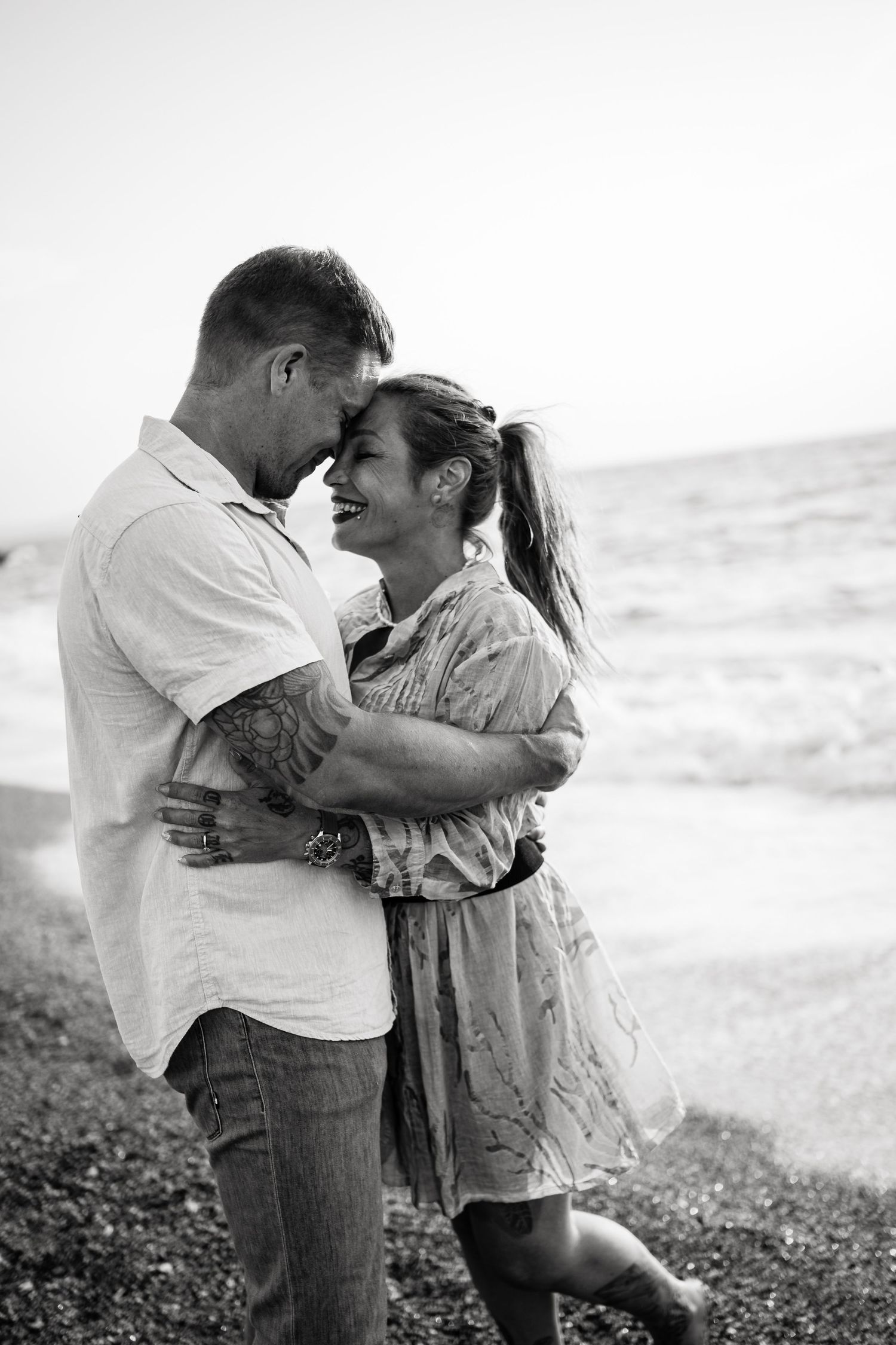 A couple shares tender moments on a rocky beach with waves in the background.