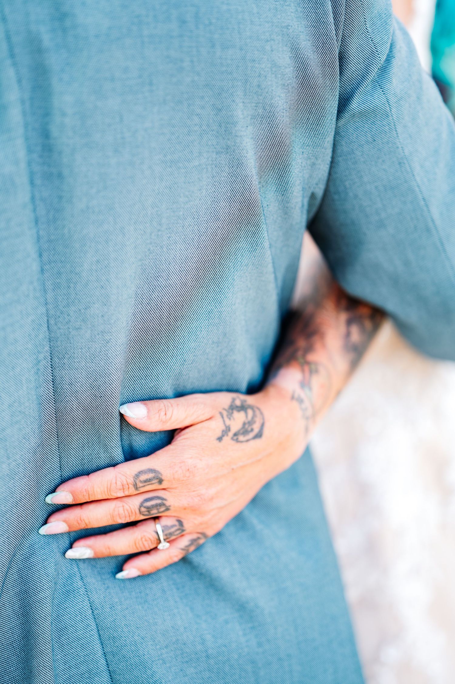 Close-up sequence of a hand with tattoos against a teal colored fabric.
