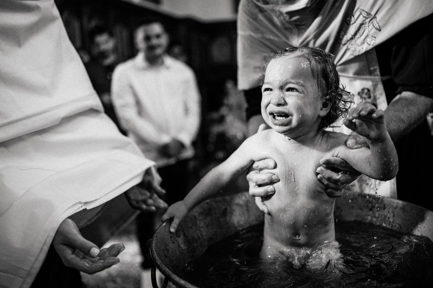 A joyful baby laughs during their baptism ceremony while being held over the font.