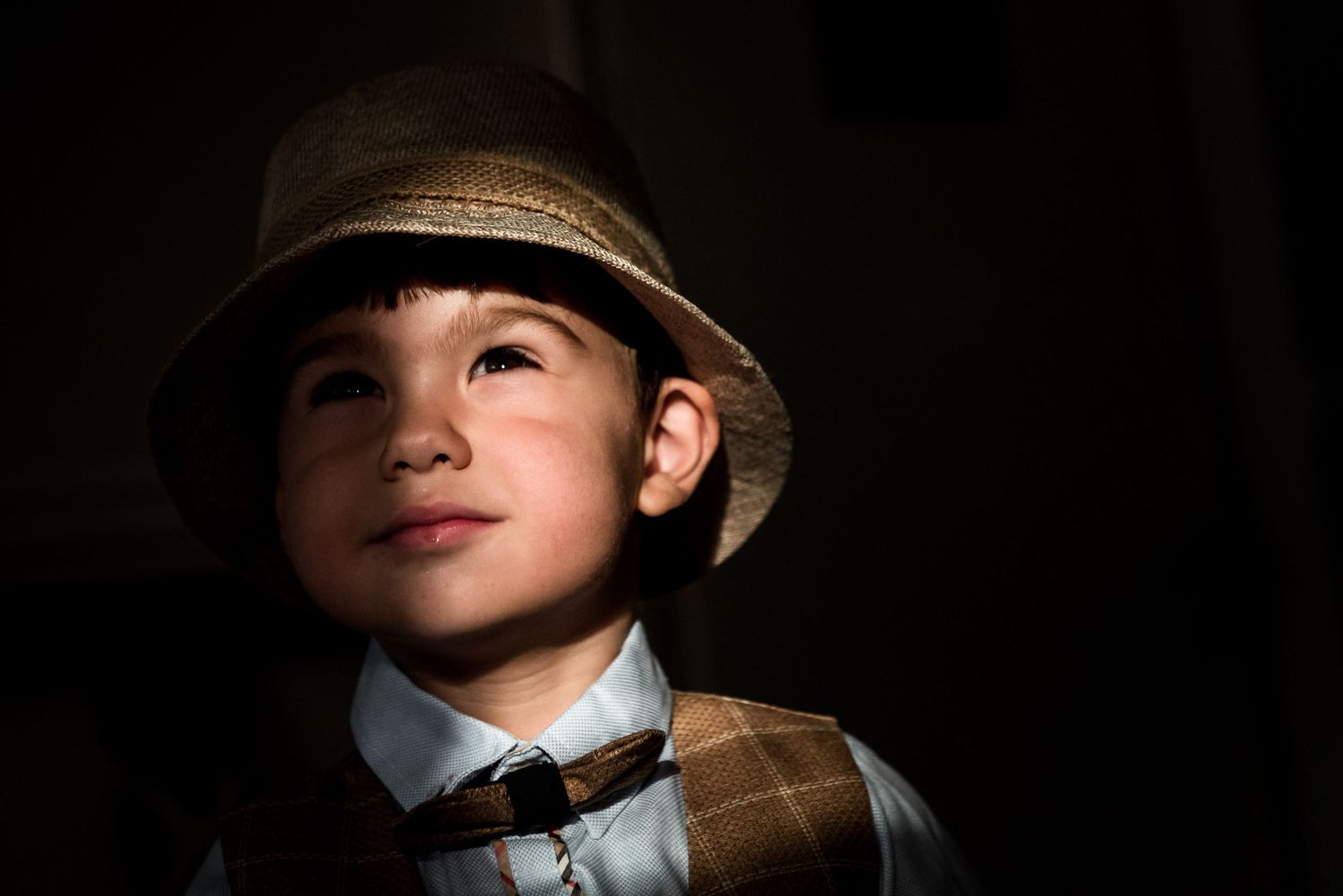 Dramatic lighting on figure wearing vintage-style hat and bowtie.