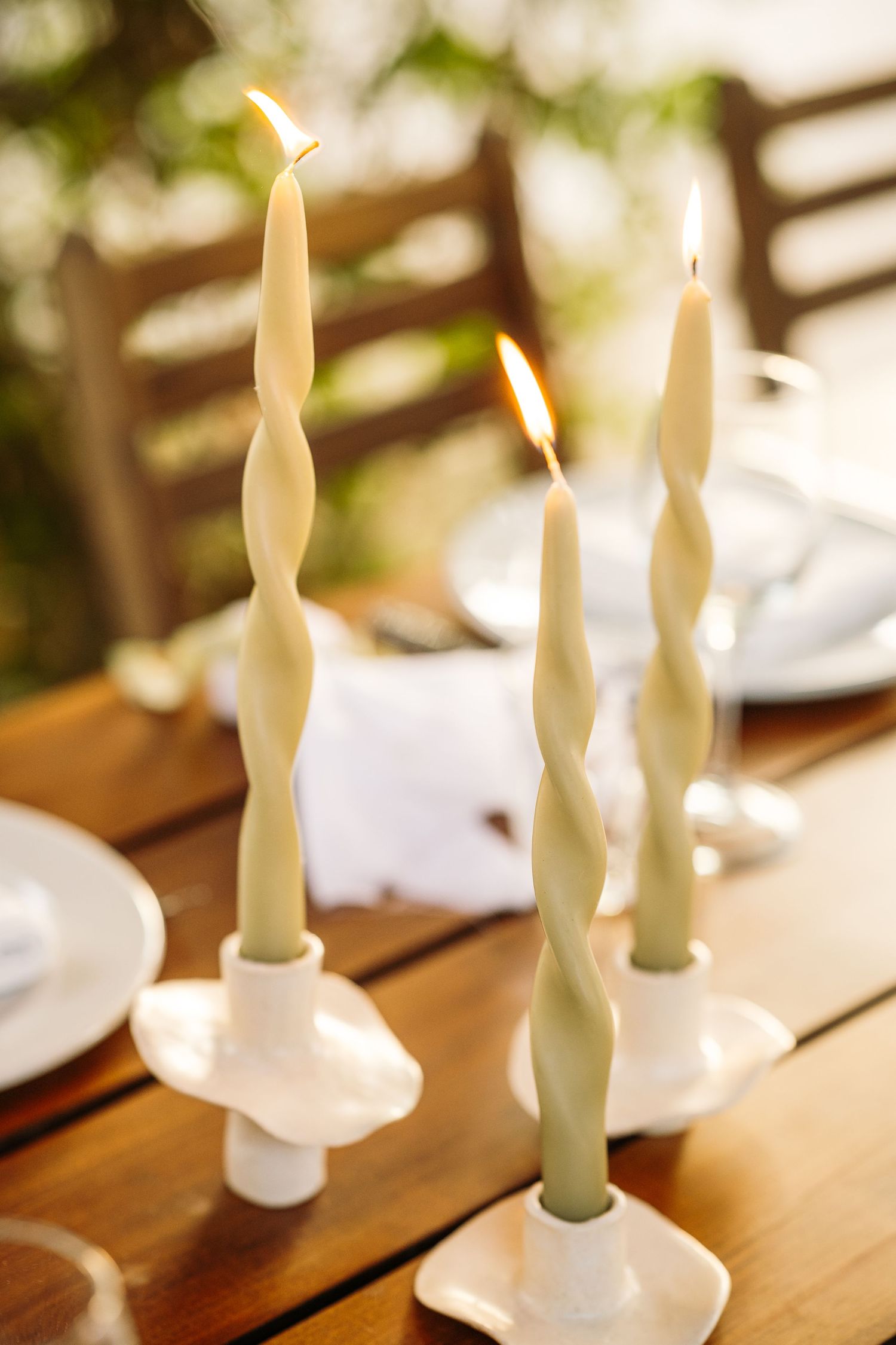 White taper candles in glass holders arranged on a wooden dining table.
