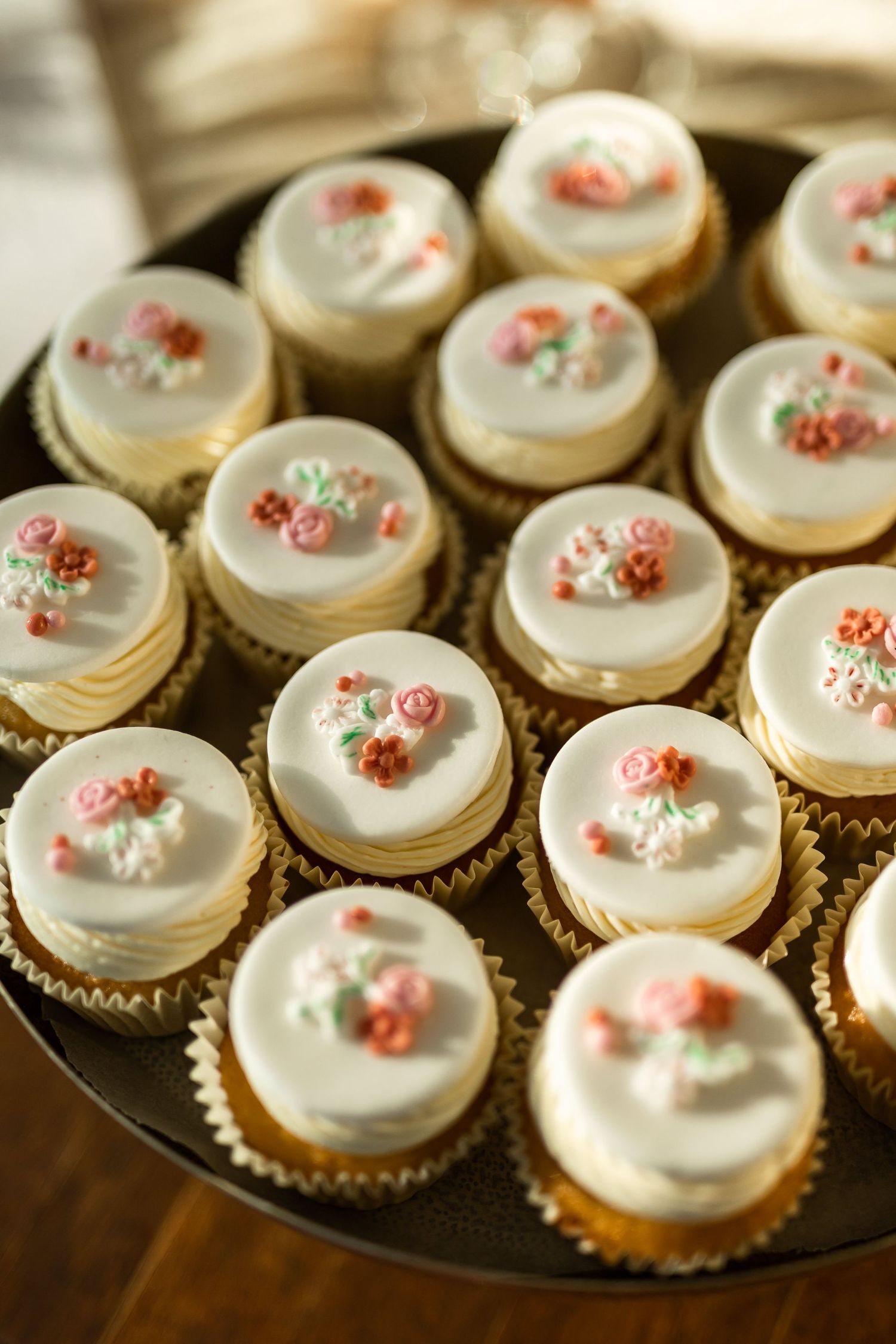Elegant white cupcakes decorated with delicate pink flowers arranged on a display tray.