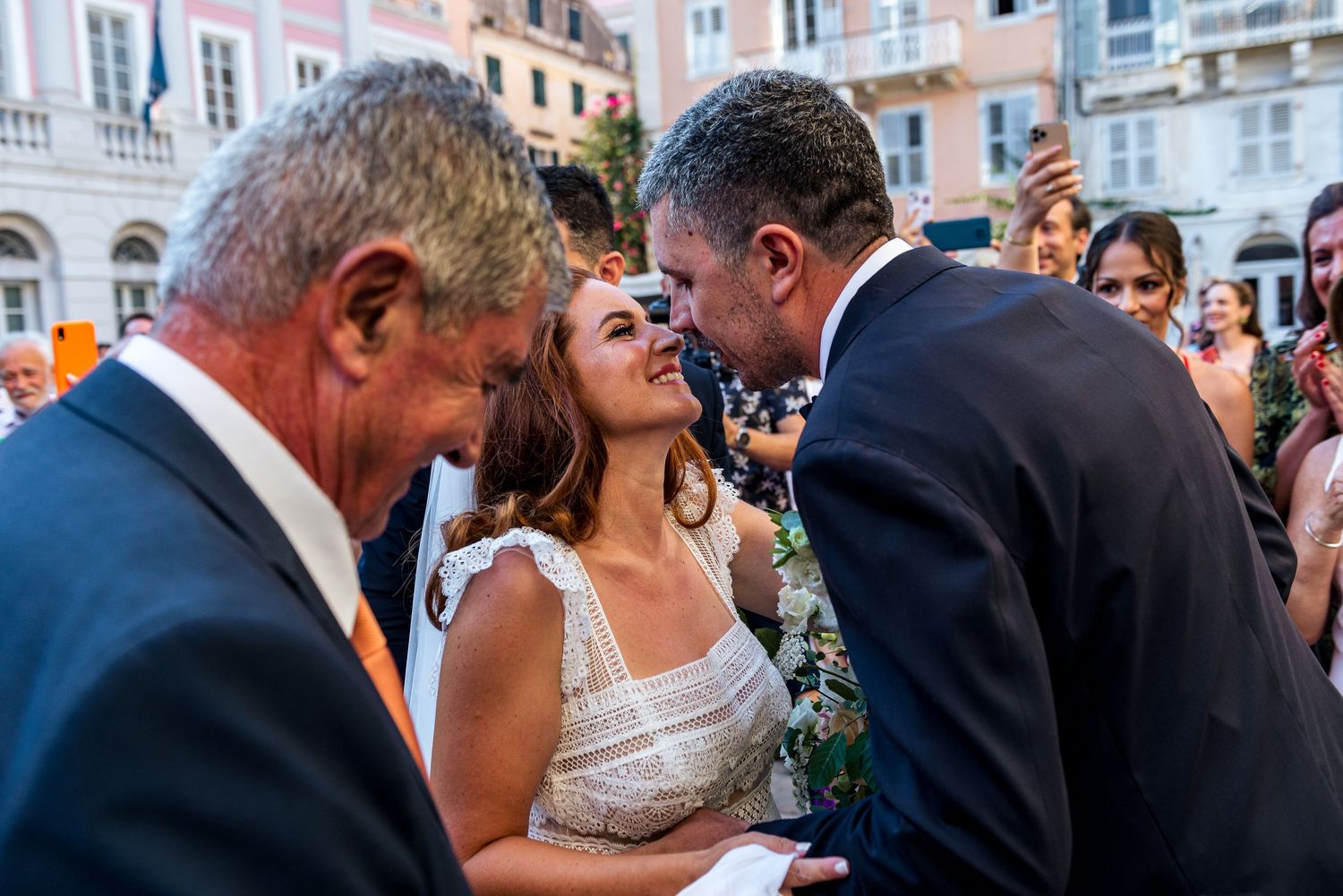 Wedding party celebrates on a European street lined with pastel buildings.