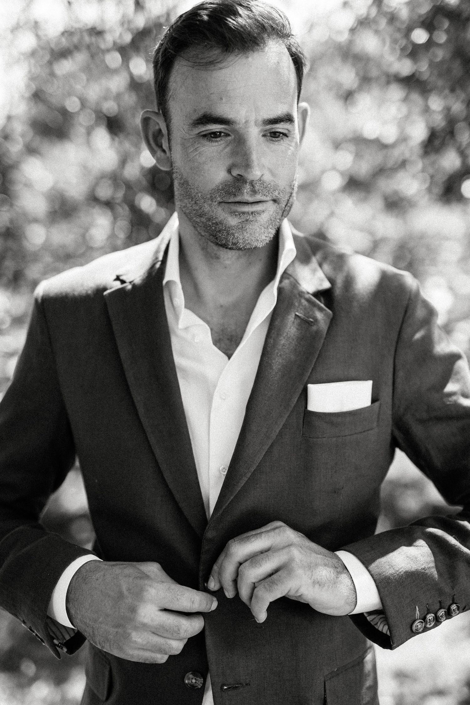 Man in dark suit jacket and white shirt adjusting his cuffs outdoors.