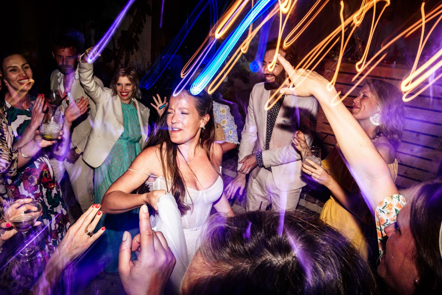 Dance floor filled with wedding guests under vibrant purple and orange lighting.