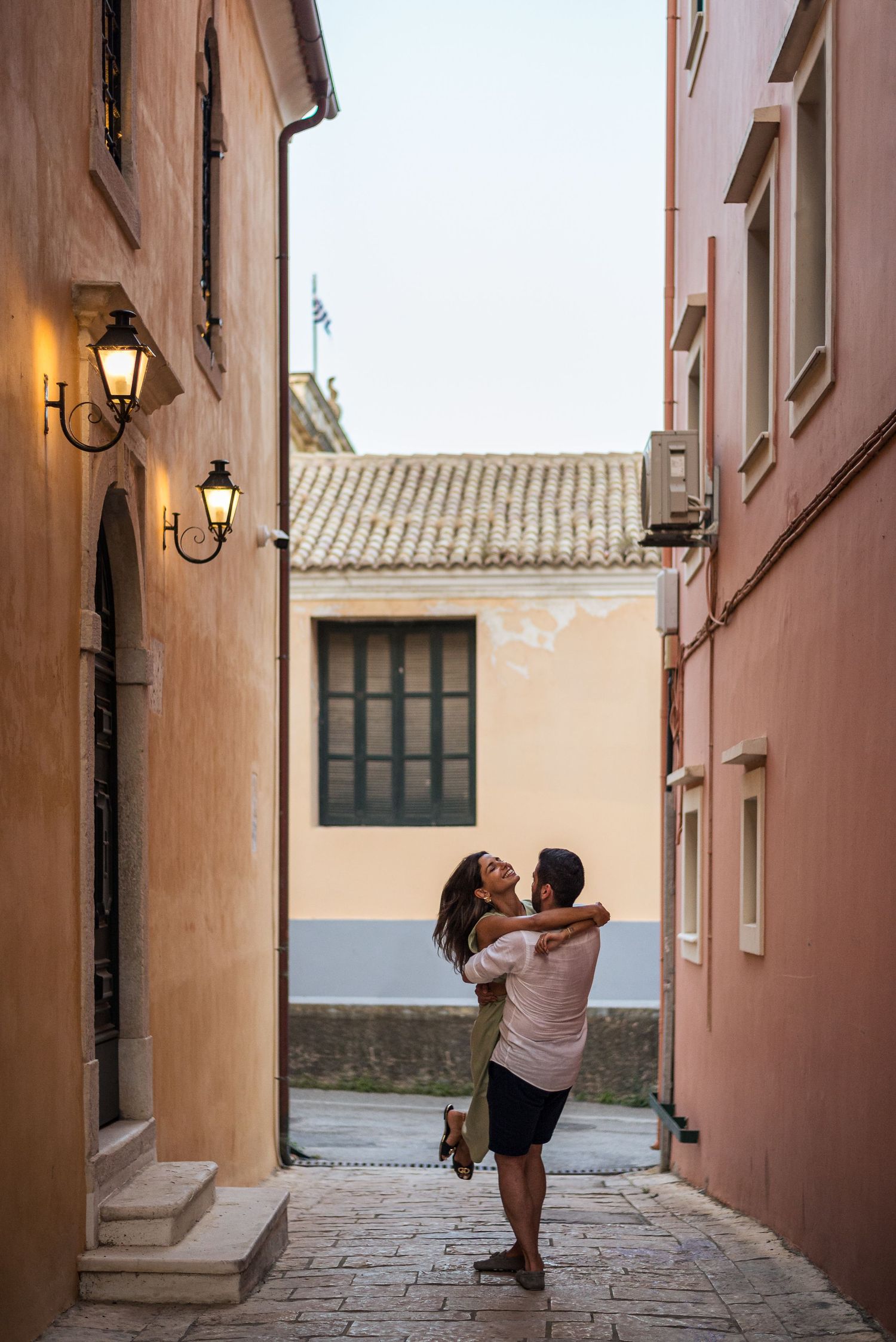 A tender embrace captured in a picturesque alleyway with warm-toned walls and vintage street lamps.