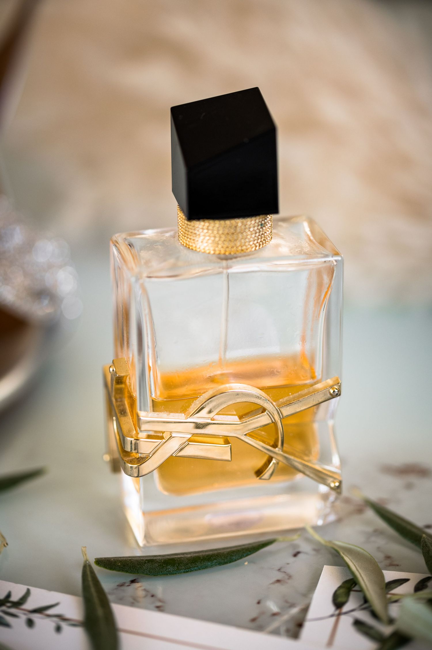 Crystal perfume bottle with gold accents photographed against a light background with greenery.