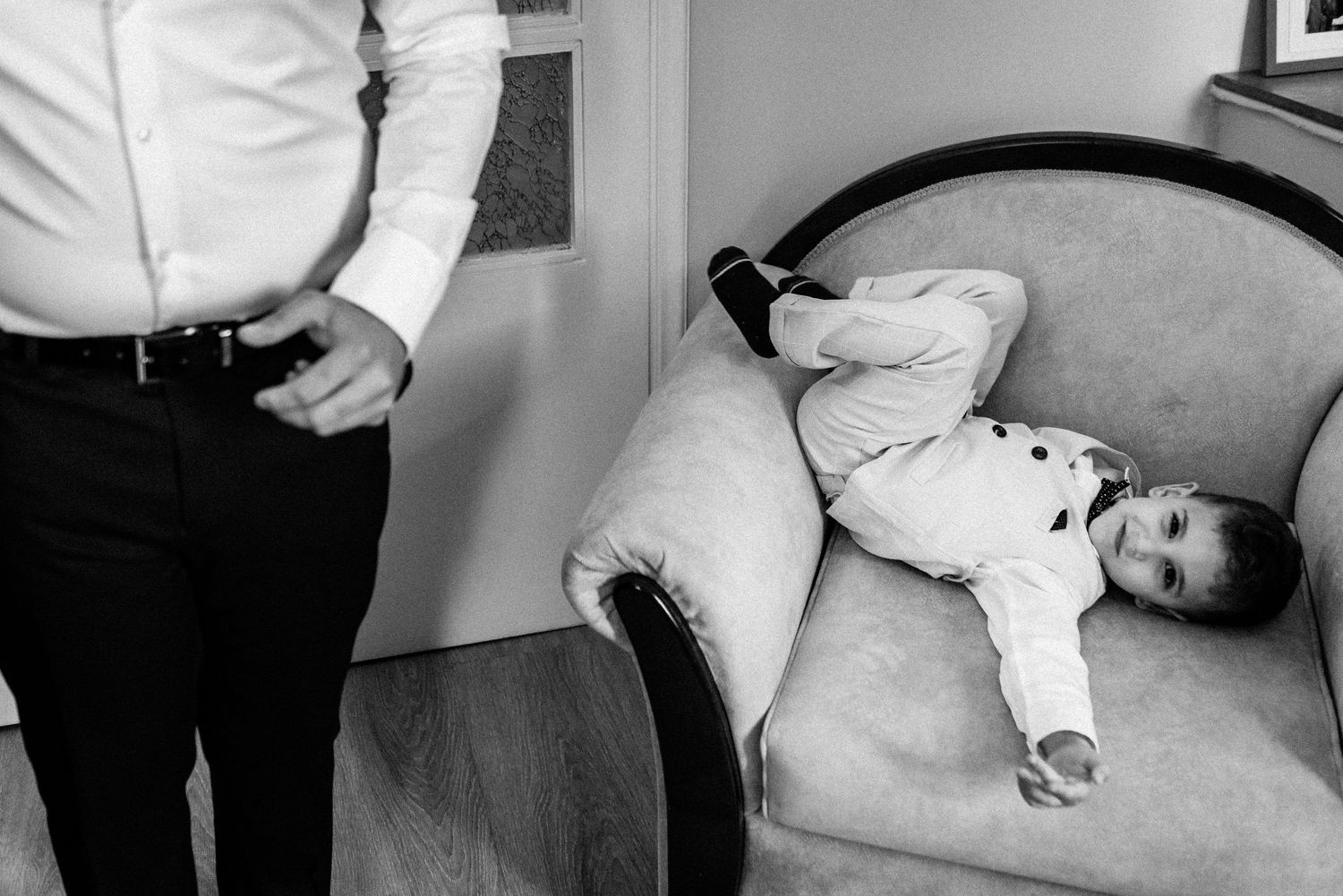 A candid black and white photo of a child laying playfully on a vintage sofa.