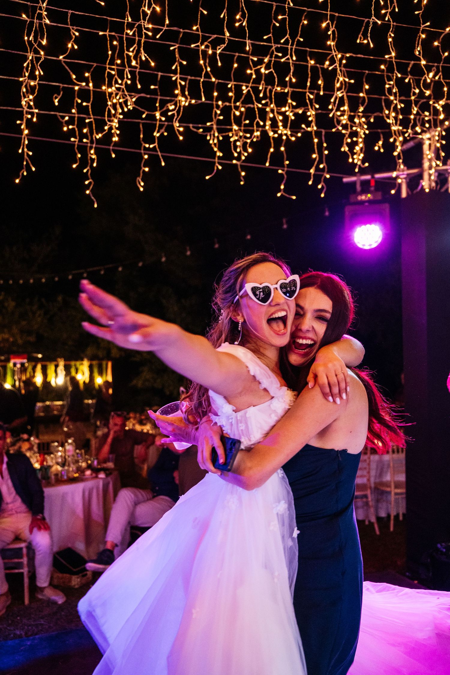 Wedding celebration under twinkling string lights with guests dancing on an outdoor dance floor.