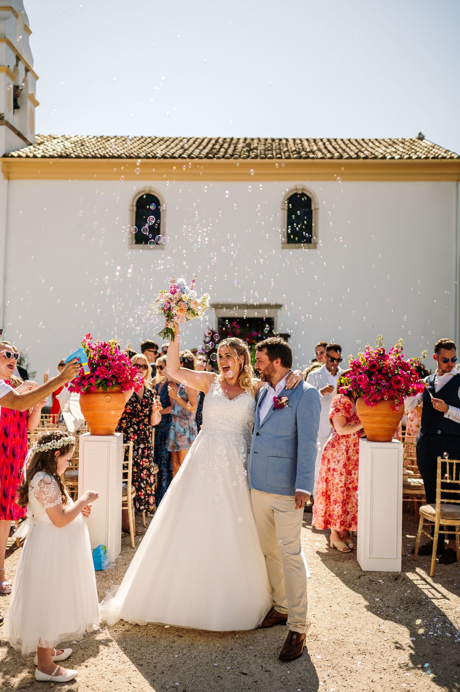 Outdoor wedding ceremony setup with white pillars and bright floral arrangements.