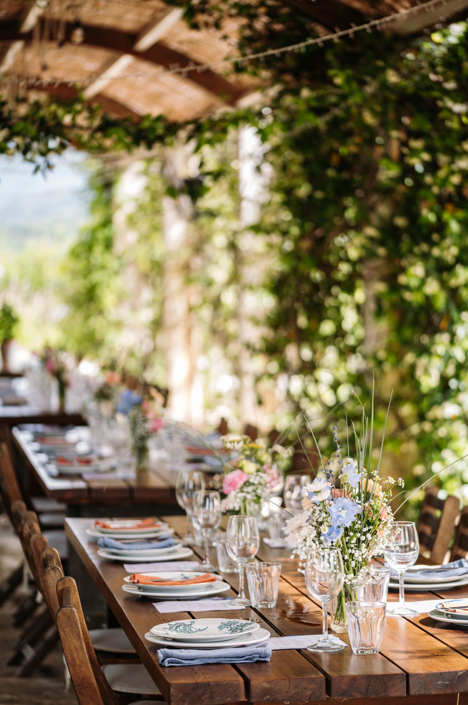 Elegant table settings arranged under a vine-covered outdoor pavilion.