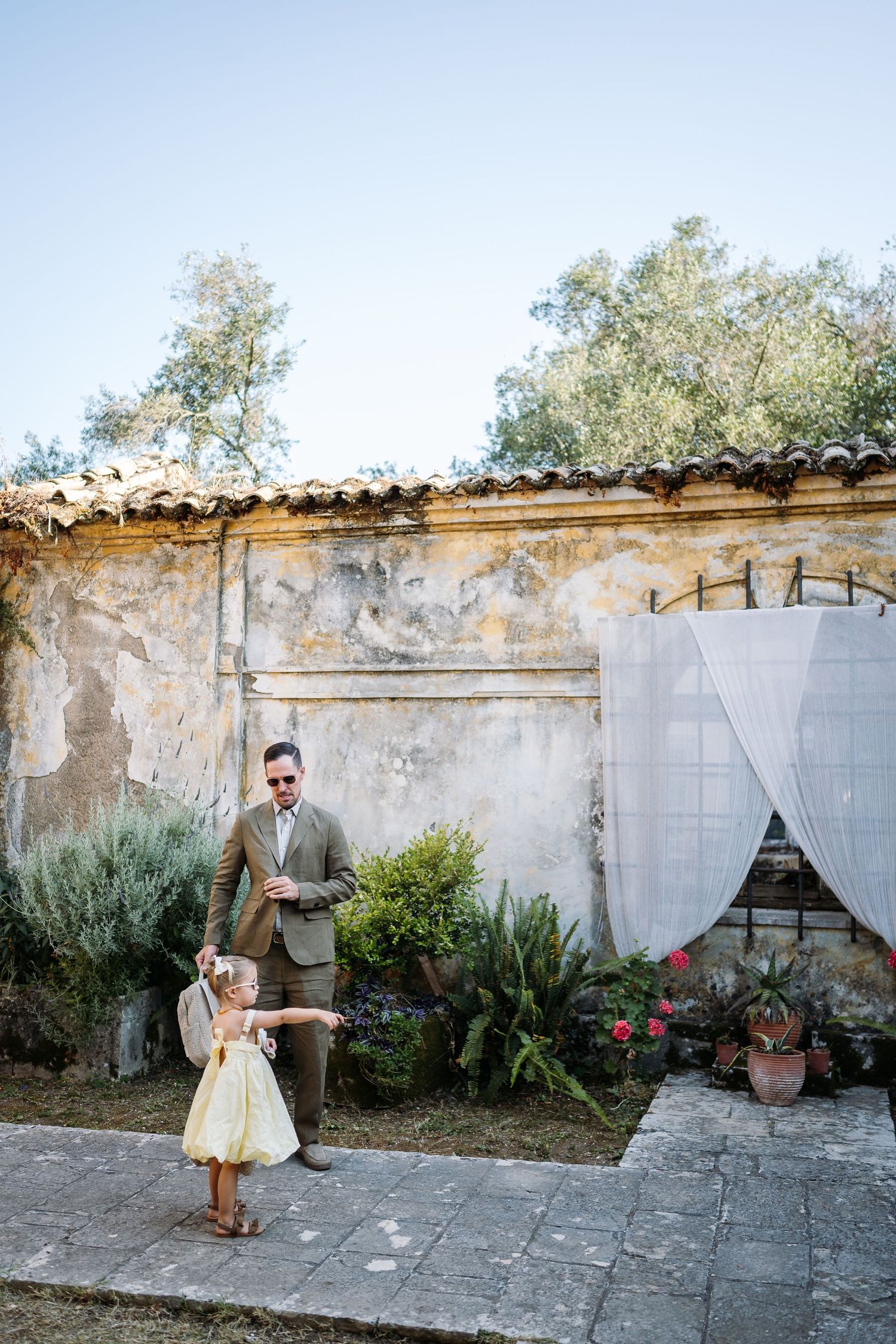 Rustic stone wall with white curtains and potted plants creates romantic garden atmosphere.