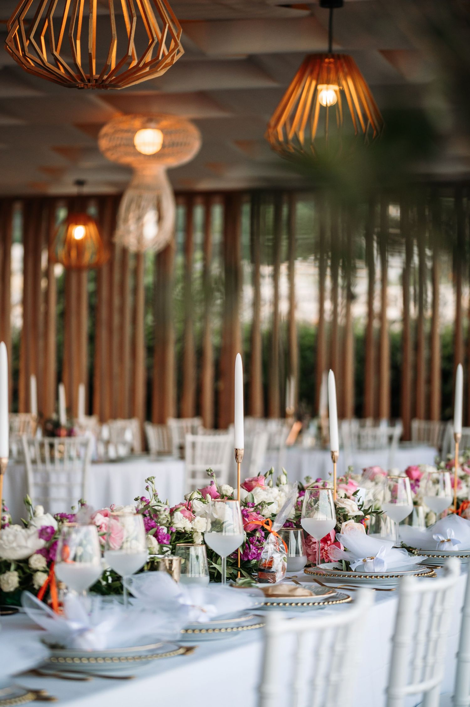 Wedding reception tables set with white linens and wooden accents under pendant lighting.