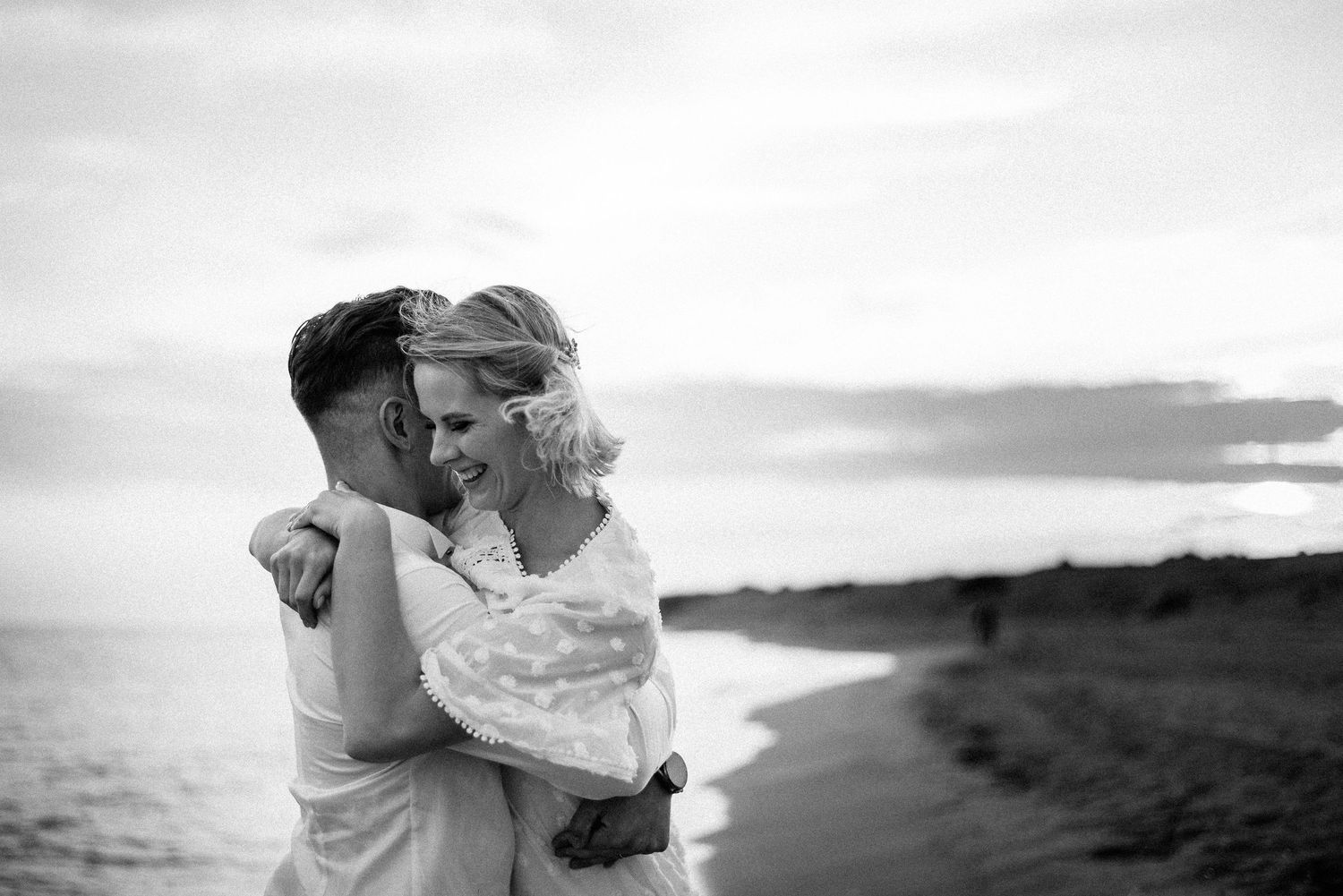 Intimate black and white photo of a couple sharing a tender moment by the ocean.