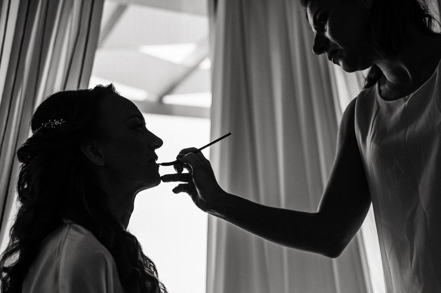 Silhouetted figures preparing for wedding day in window light.