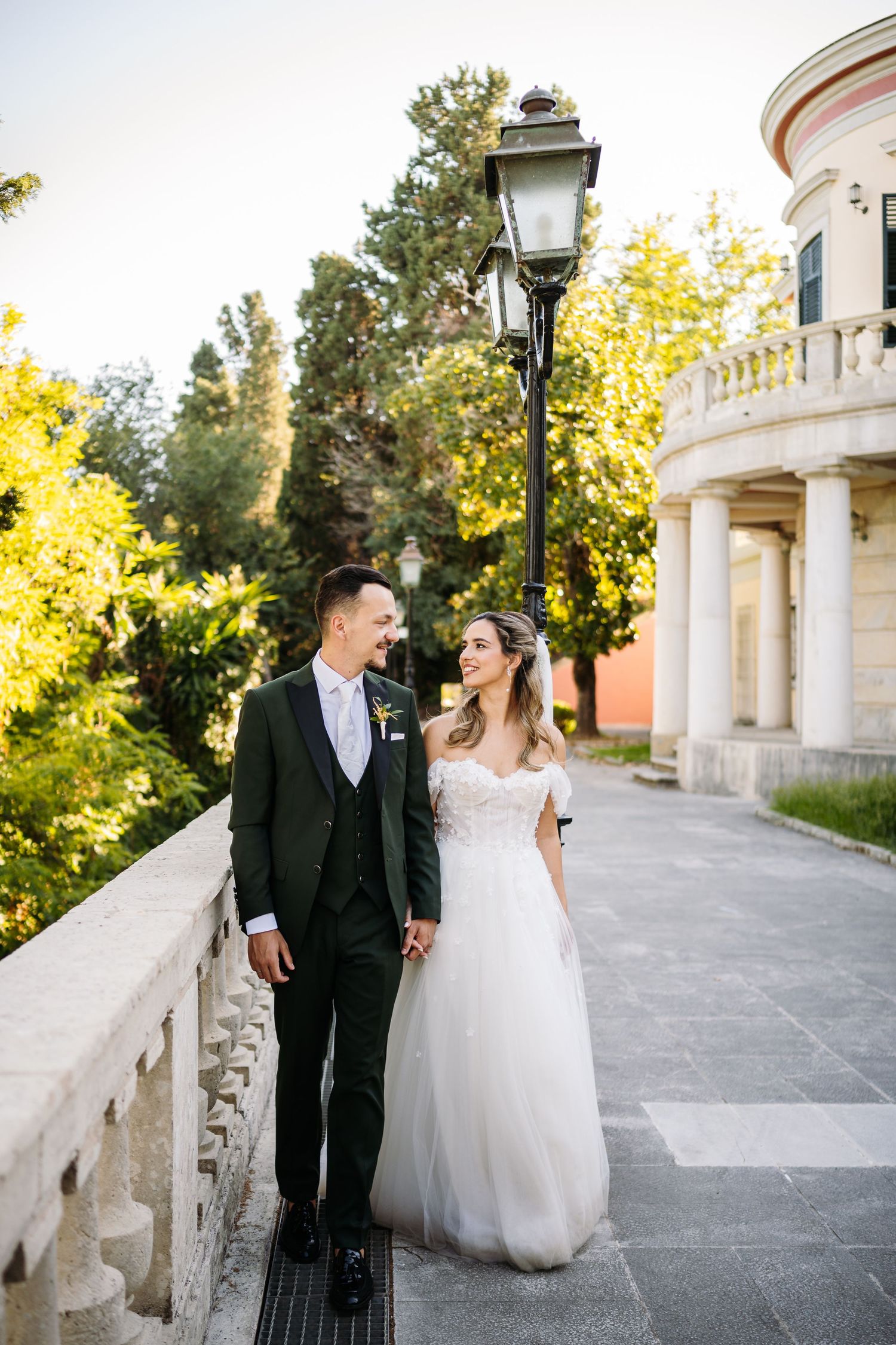 Newlyweds walk together along a beautiful outdoor colonnade pathway with ornate architecture.