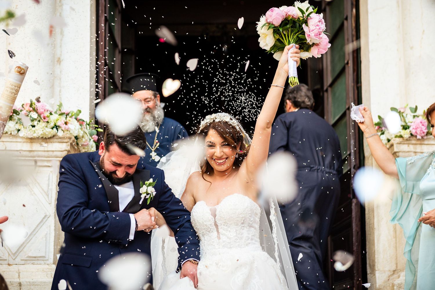 Wedding party celebrates outside a historic venue with pink floral decorations.