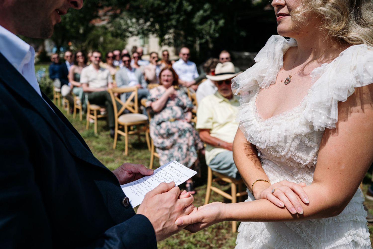 Wedding couple exchanges rings during an intimate outdoor ceremony surrounded by guests.
