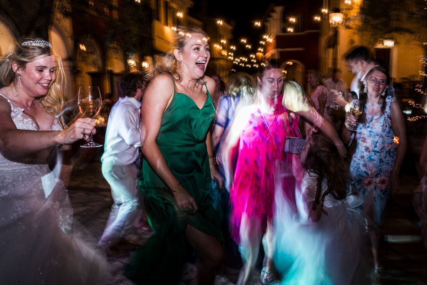 Wedding guests dancing energetically under colorful disco lights at an evening reception.