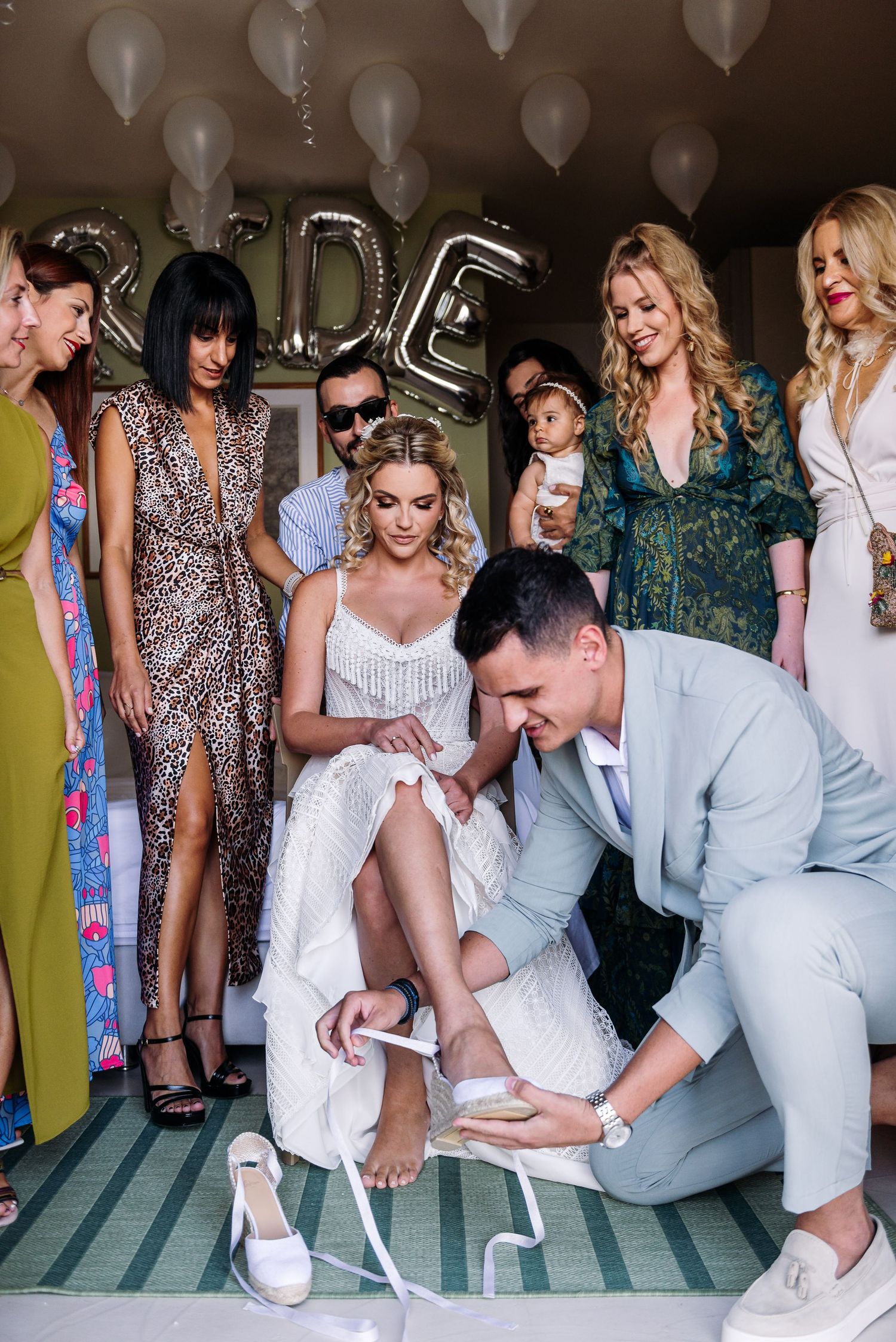 Wedding party in light colored attire sitting on a wooden deck with white balloons overhead.