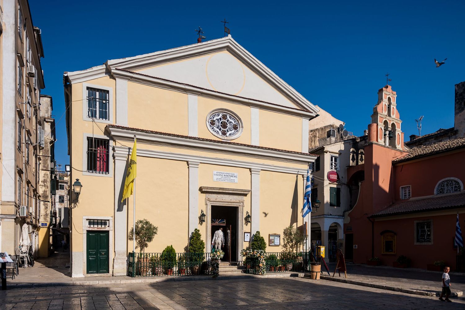 Panoramic view of a yellow church building against bright blue sky.