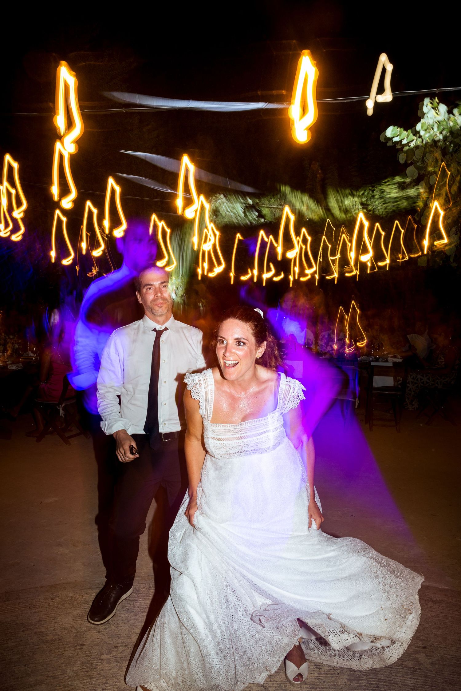Motion-blurred dancers move under glowing string lights with purple lighting effects.