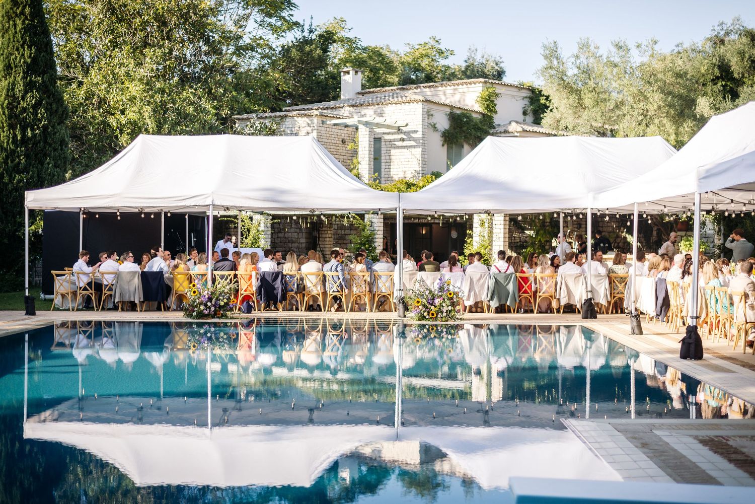 Panoramic view of white wedding tents set up alongside a swimming pool for an outdoor celebration.