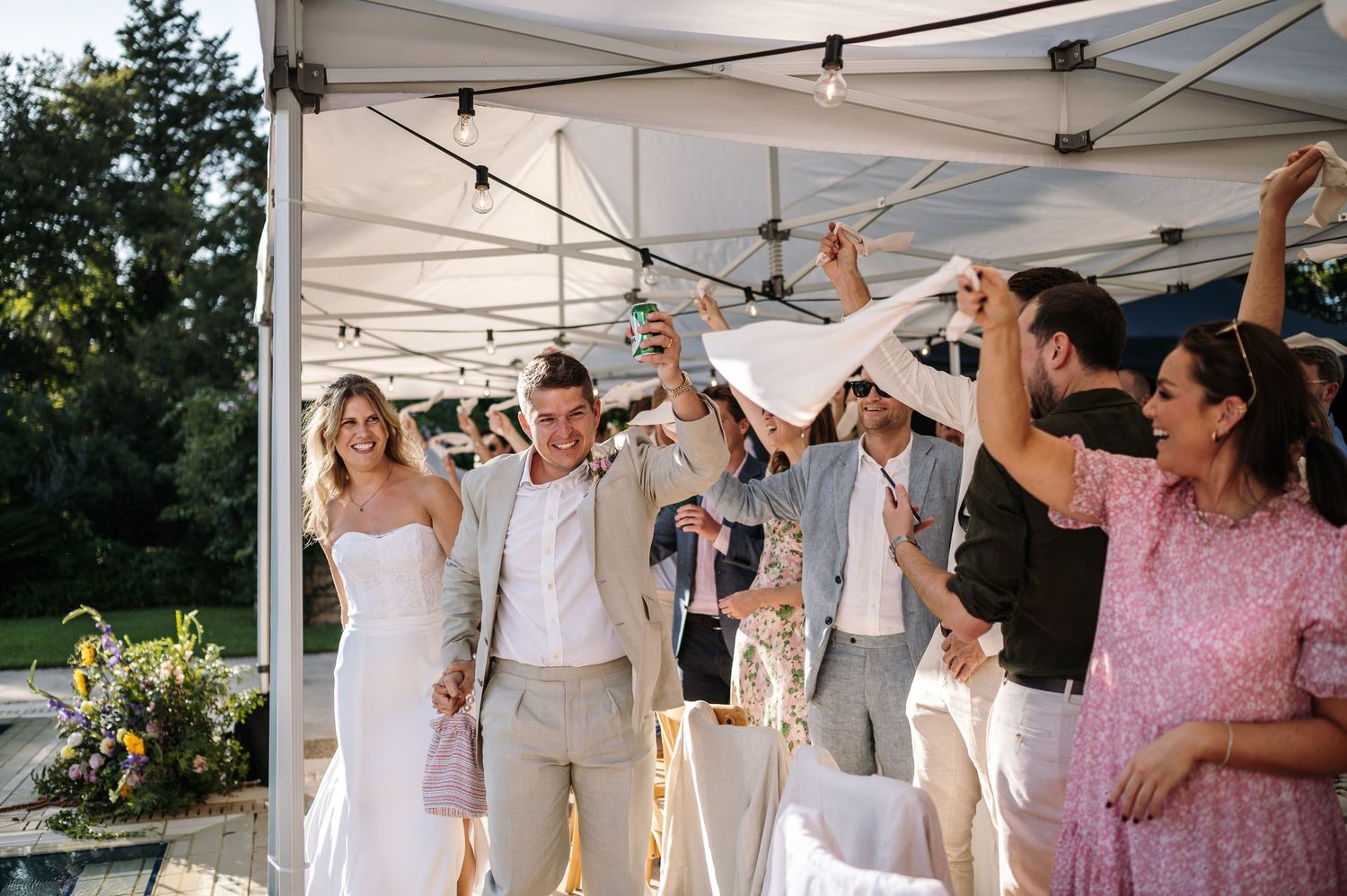 Wedding guests celebrate under a white tent canopy during an outdoor reception.