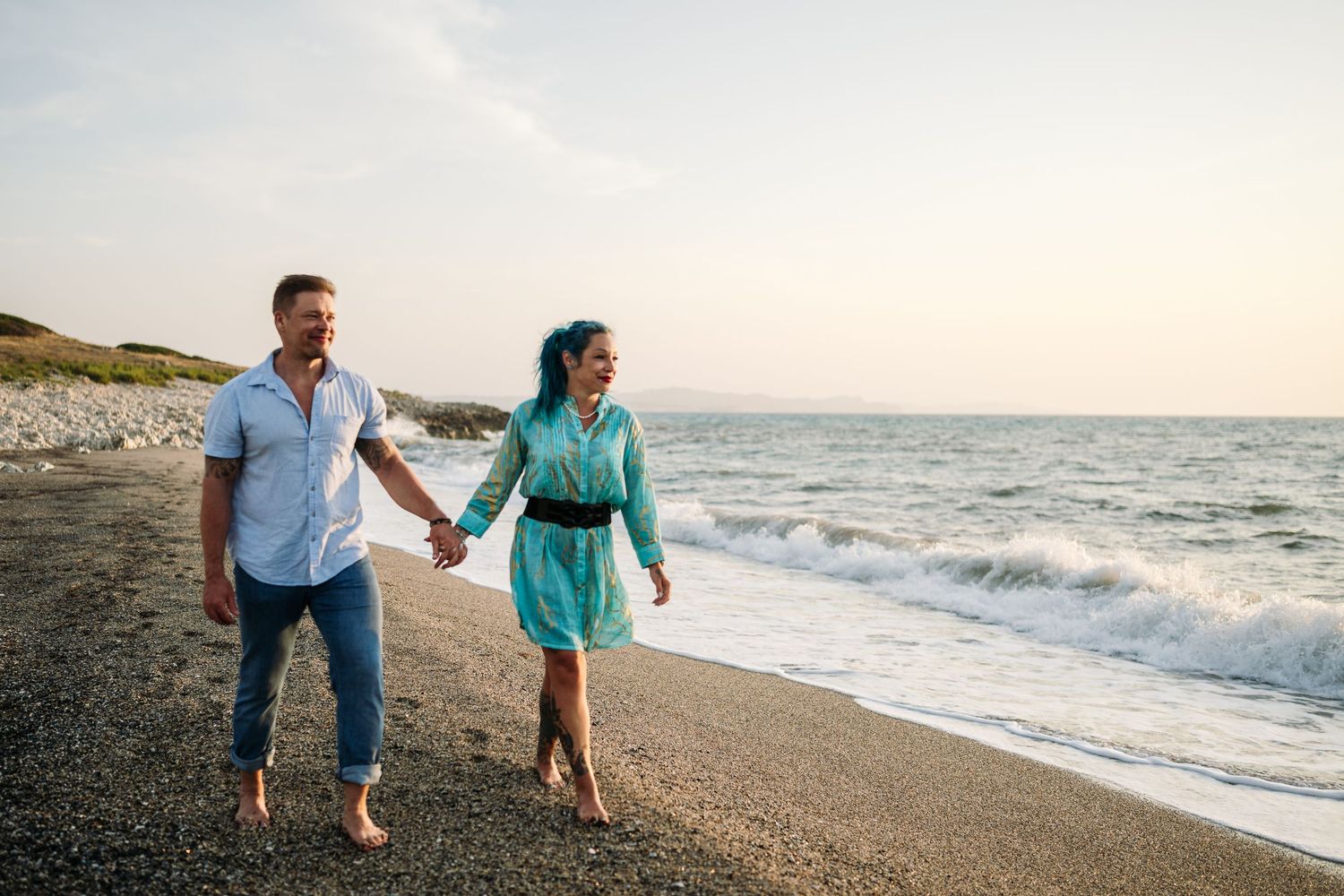 A couple strolls along a scenic beach shoreline during golden hour.