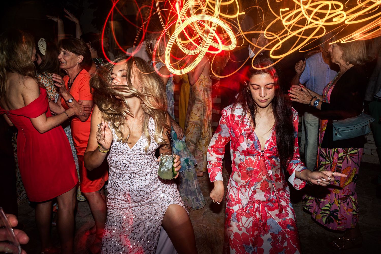 Party guests dancing and celebrating on a crowded dance floor with vibrant red lighting effects.