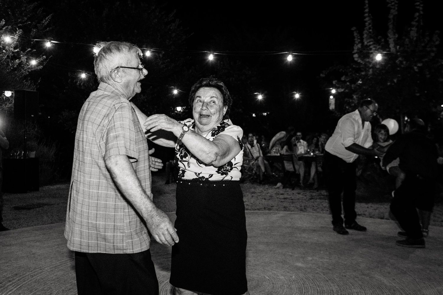Black and white photo of wedding guests dancing at an outdoor reception.