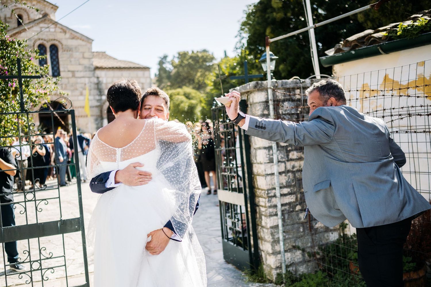 Newlyweds celebrating outside stone church gates on a sunny afternoon.