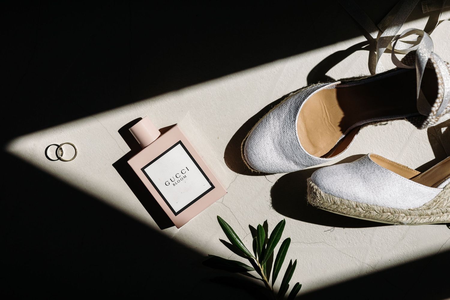 Wedding accessories including shoes and perfume arranged in dramatic lighting.