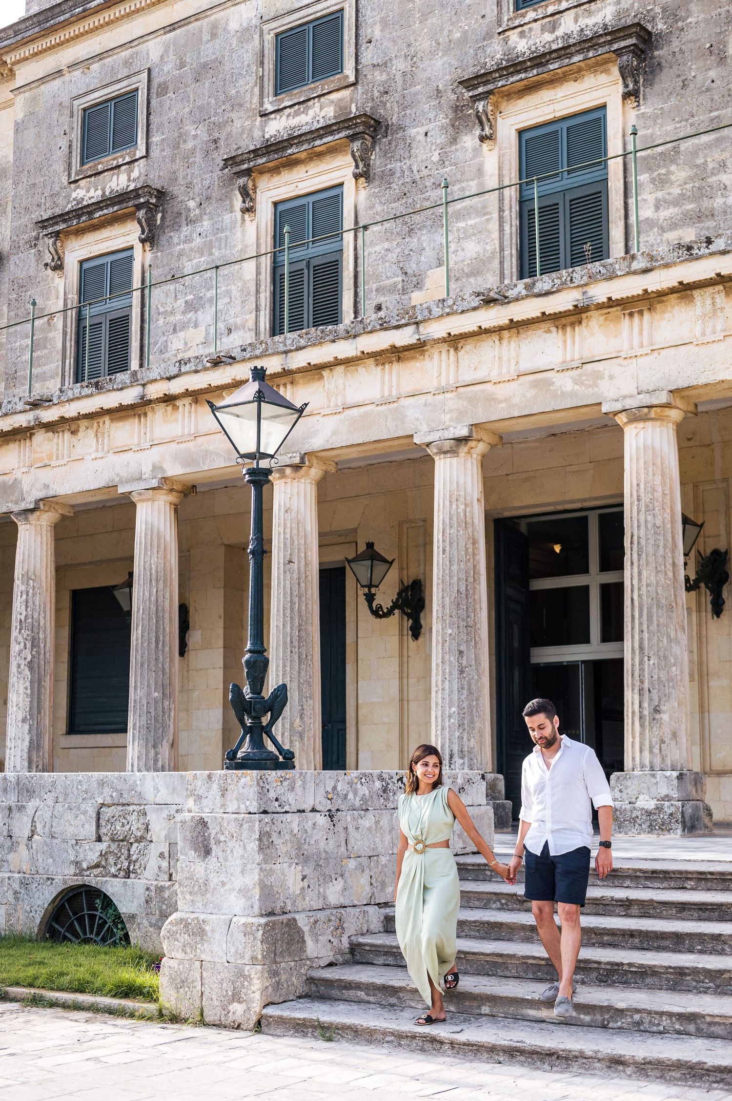 A couple explores the exterior of a historic building with white columns and stone steps.