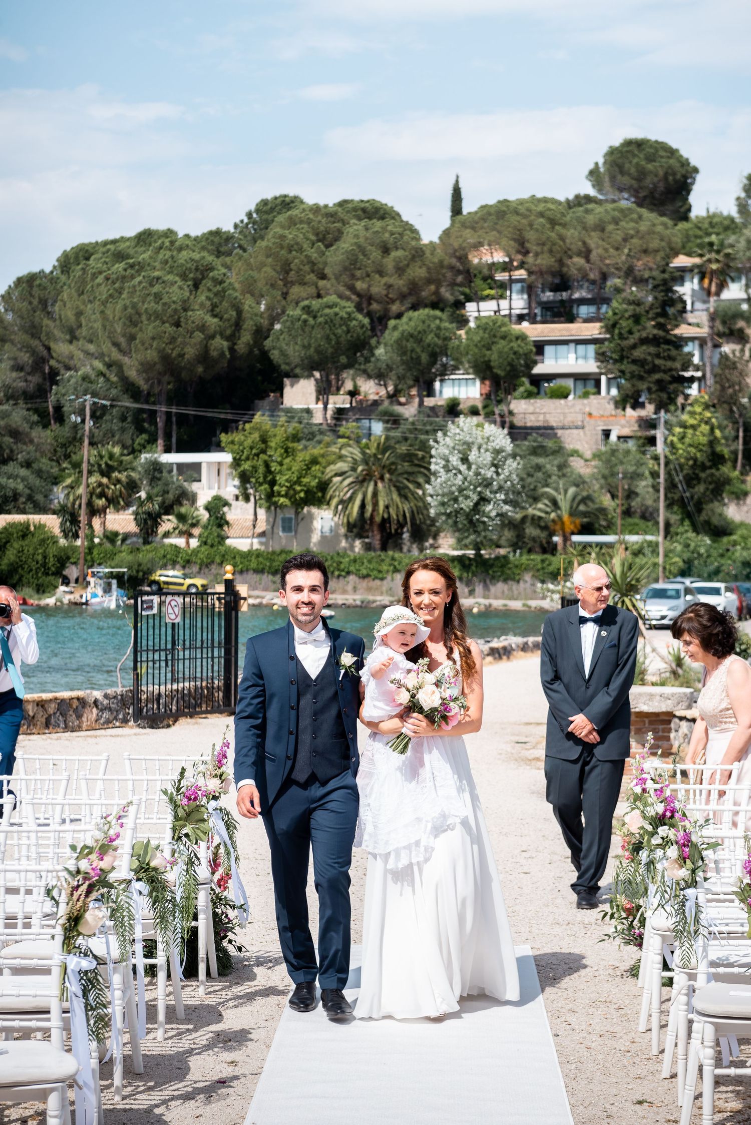 Beachfront wedding ceremony setup with white chairs and floral decorations along the shoreline.
