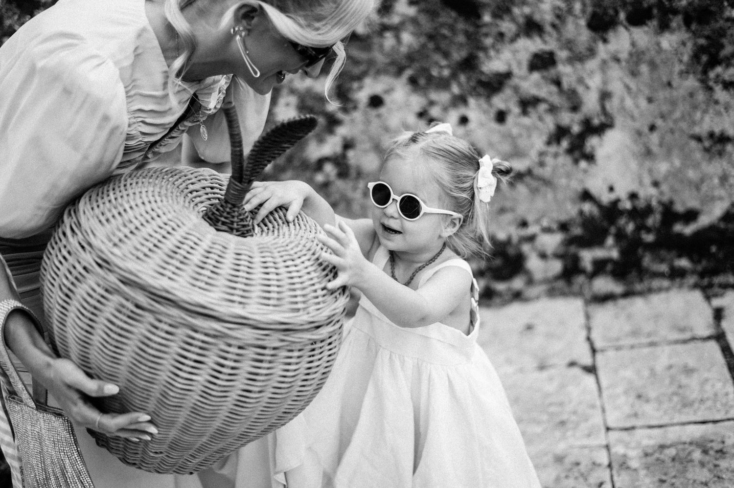 Black and white photo of a wicker basket being held near a small child in white dress.