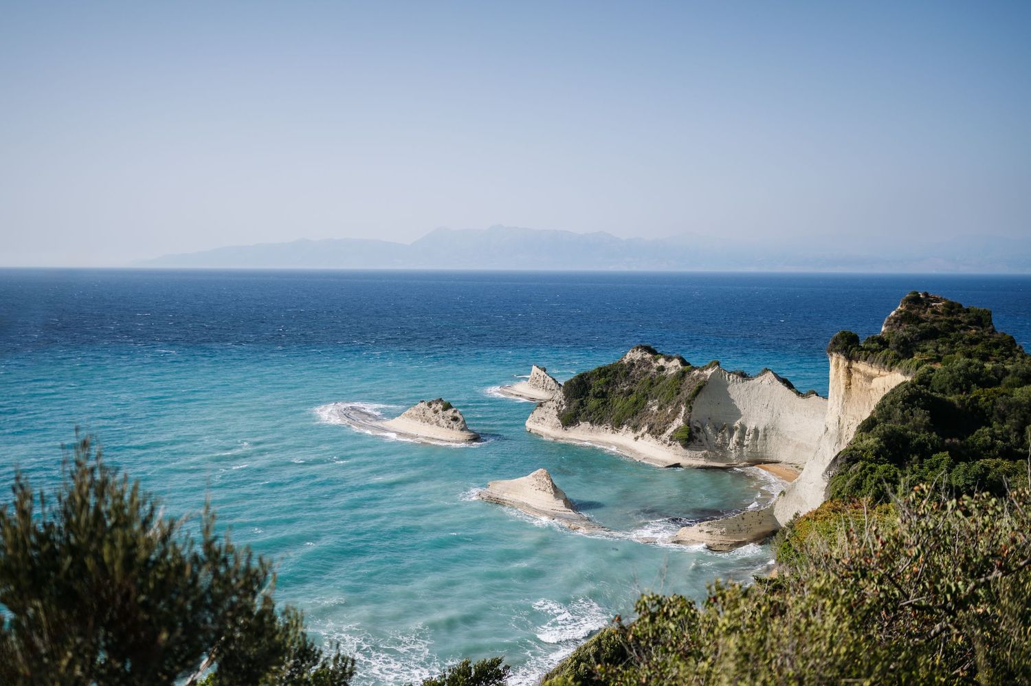 Dramatic coastal landscape with white cliffs and turquoise ocean waters under a bright blue sky.