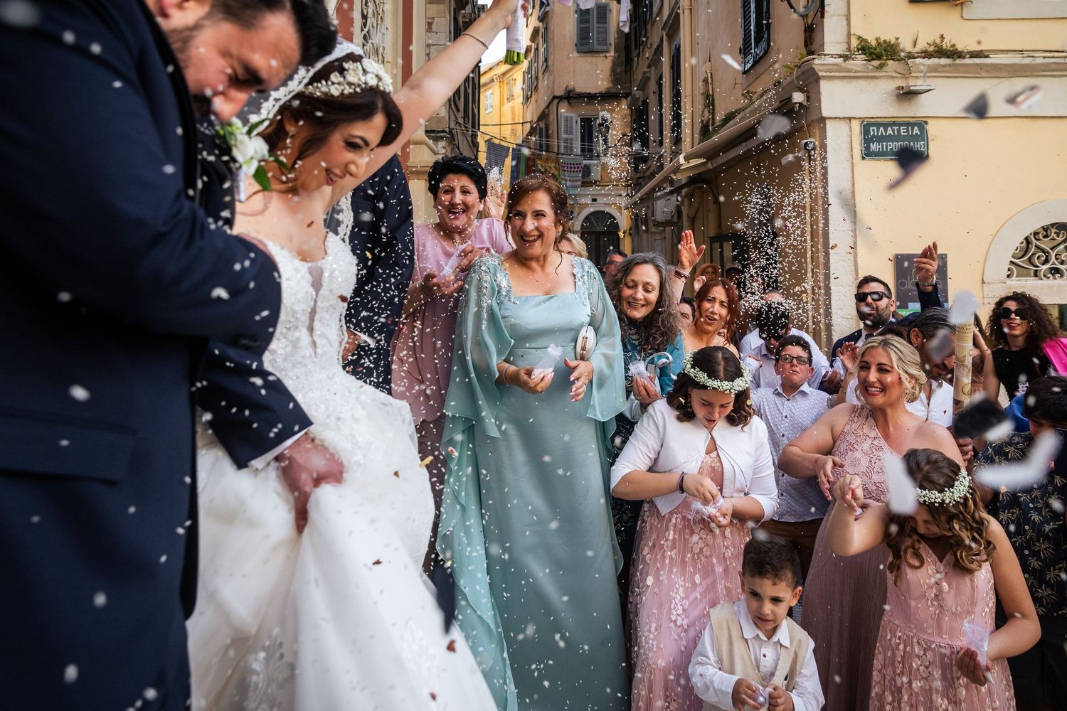 Guests celebrate with confetti as newlyweds exit a historic venue with pink floral arrangements.