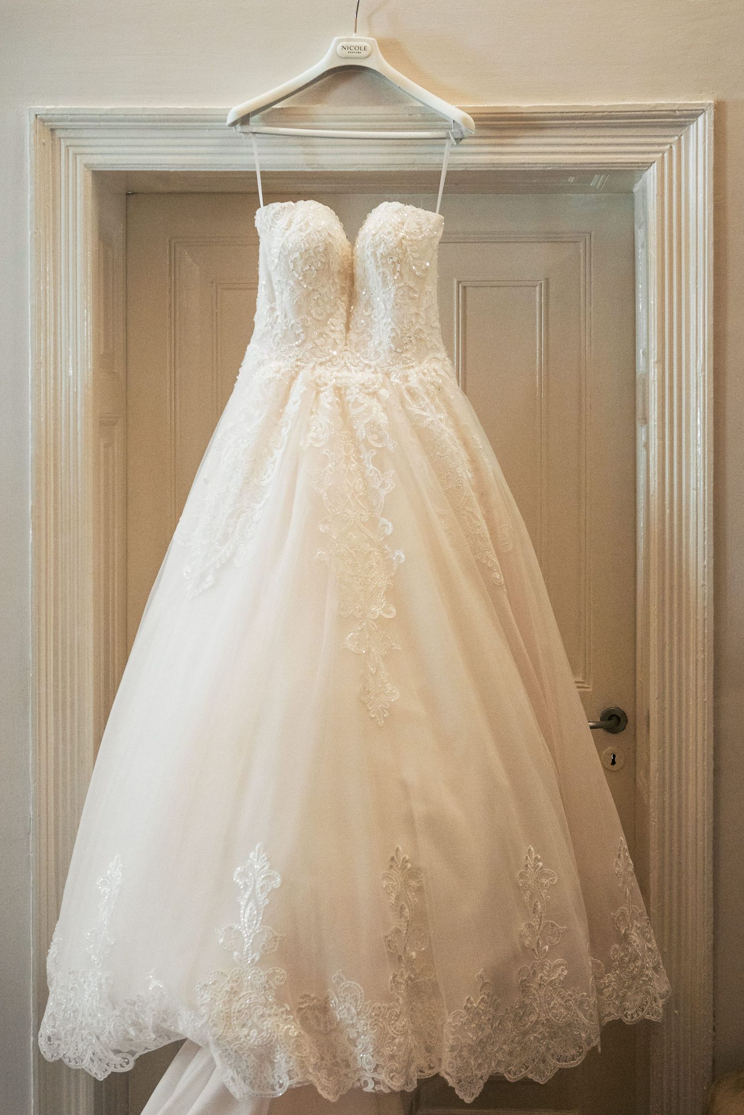 A white lace wedding dress with sweetheart neckline hangs on display in a doorframe.