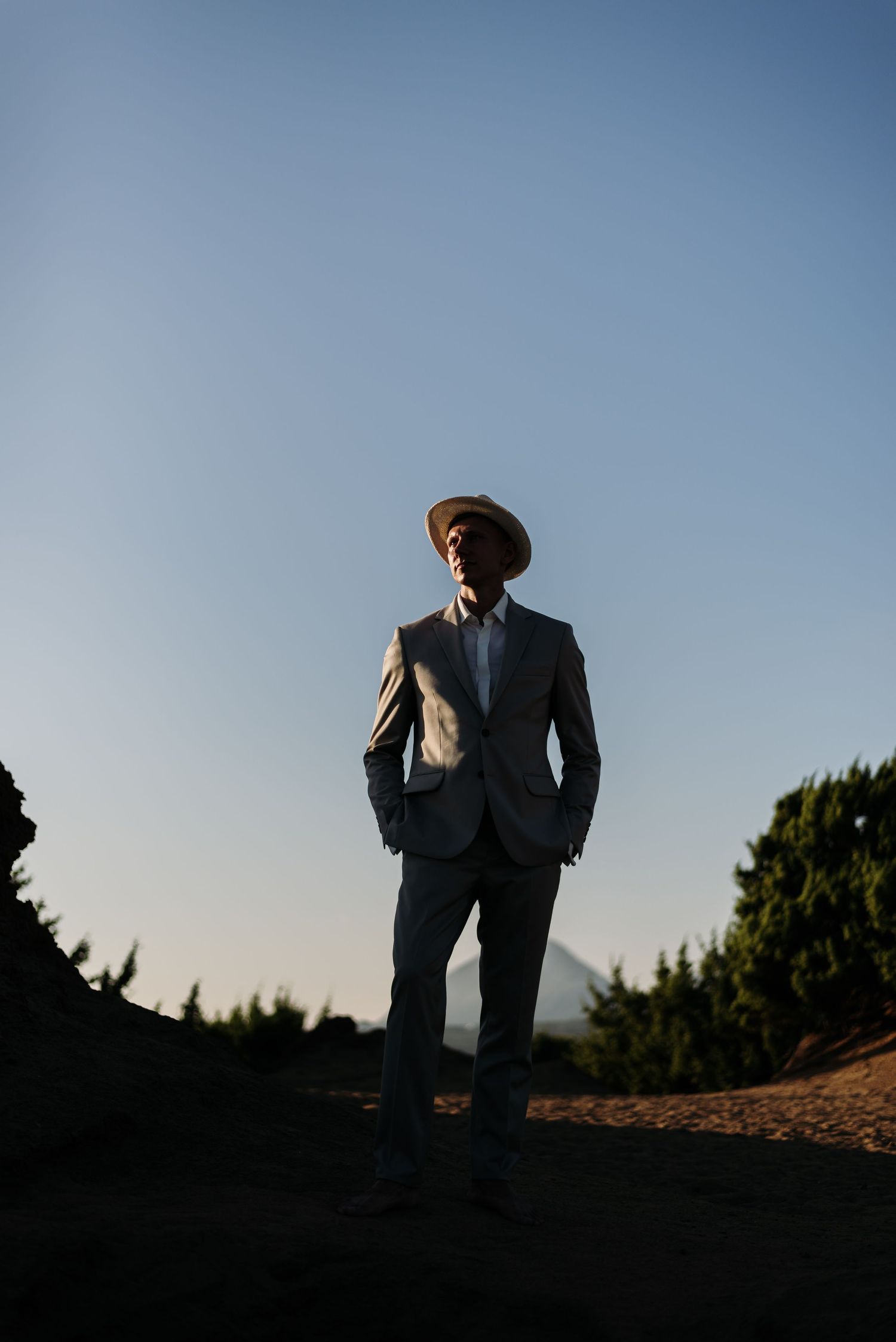 Silhouetted figures in formal attire stand against a blue sky during sunset at an outdoor location.