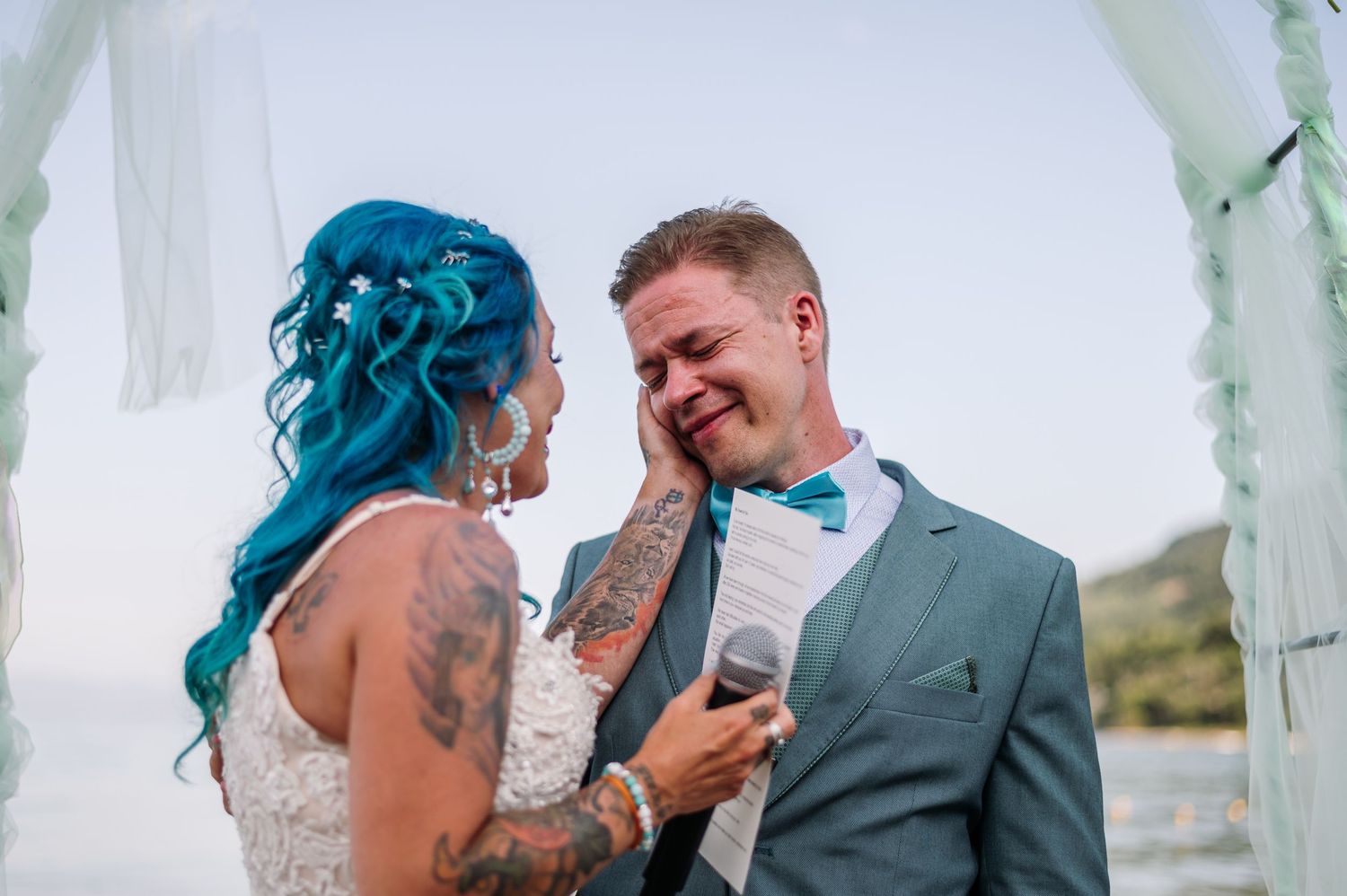 A couple shares an intimate moment during their beach wedding ceremony, with the bride wearing a white lace dress.